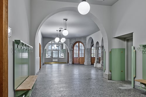 Flur mit Bögen und grossen Fenstern, helle Lichtakzente.