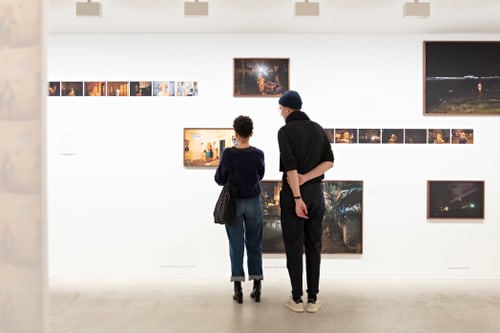 Zwei Personen betrachten Fotografien an einer Galeriewand.
