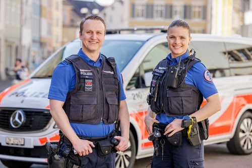 Zwei Polizisten in blauer Uniform vor einem Polizeiauto.