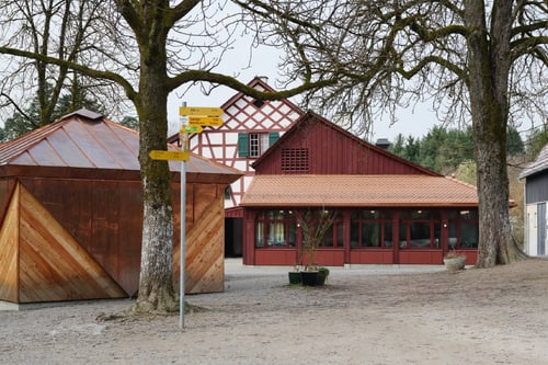 Traditionelles Gebäude mit roten Akzenten und Bäumen im Vordergrund.
