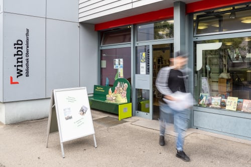 Aussenansicht Bibliothek Oberwinterthur. Person geht an Schaufenstern vorbei.