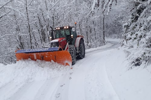 Traktor räumt Schnee auf verschneiter Strasse.