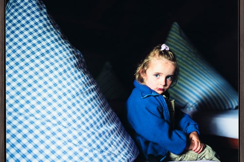 Kind in einem blauen Pullover sitzt neben einem grossen gestreiften Kissen.