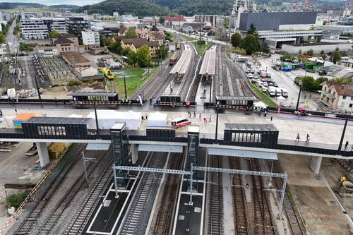 Luftaufnahme eines Bahnhofs mit mehreren Gleisen und Gebäuden im Hintergrund.