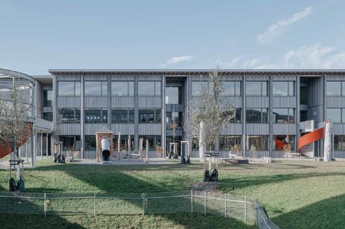 Moderne Schulgebäude mit Spielplatz im Vordergrund.