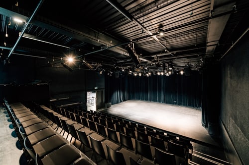 Kleiner leerer Theatersaal mit Bühne und Sitzreihen.