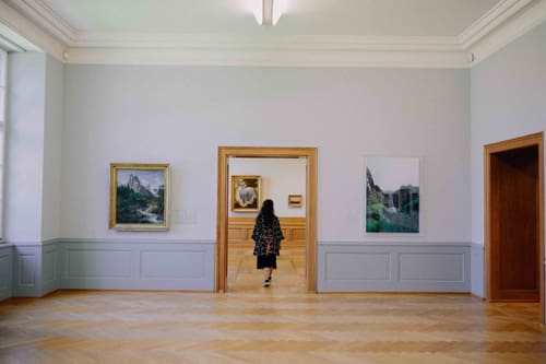 Kunstgalerie mit Gemälden an den Wänden, Person im Hintergrund.