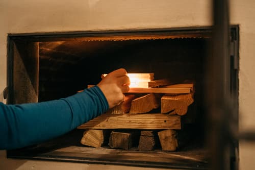 Person in blauem Ärmel zündet Holz im Ofen an.