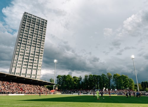 Fussballspiel vor hoher Gebäudekulisse.