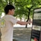 Person im weissen T-Shirt zeigt auf Infotafel in einem Park.