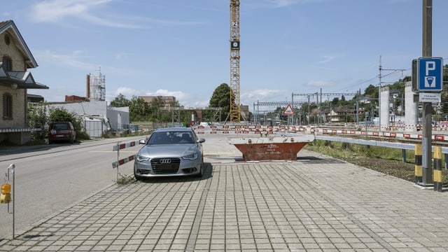 Auto auf gepflastertem Parkplatz neben Baustelle und Baukran.