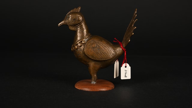 Metallfigur eines Vogels mit Etiketten auf dunklem Hintergrund.