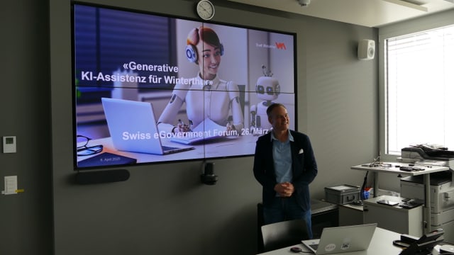 Person steht neben einem digitalen Präsentationsbildschirm in einem Büro.