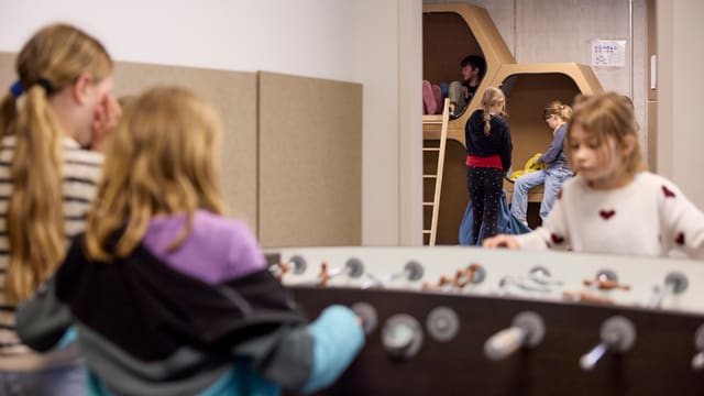 Kinder spielen Tischfussball und klettern in einem Innenraum.