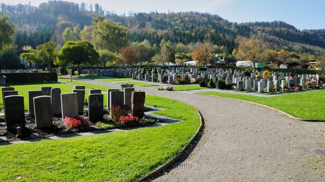 Friedhof mit Grabsteinen und Bäumen in herbstlicher Landschaft.