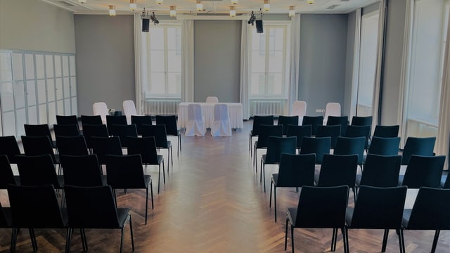 Konferenzraum mit Stuhlreihen und Tisch vorne.