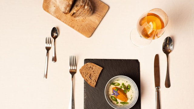 Gedeckter Tisch mit Brot, Suppe und Besteck.