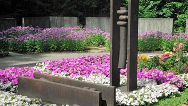 Metallskulptur in einem Garten mit bunten Blumen.
