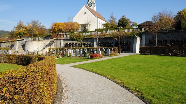 Friedhof mit Kiesweg und Kirche im Hintergrund.