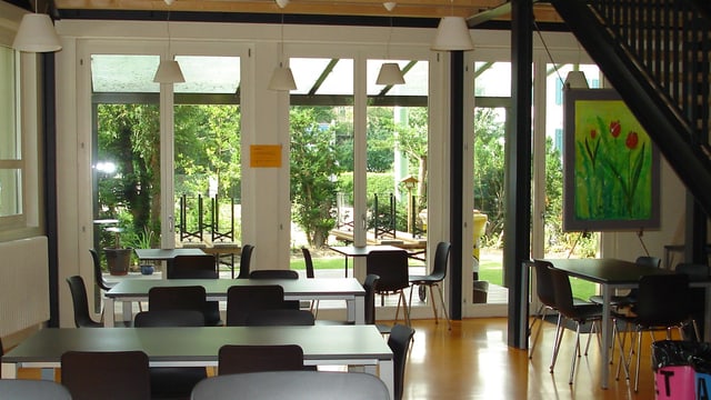Ein leerer Gemeinschaftsraum mit Tischen und Stühlen, Blick nach draussen in den Garten.