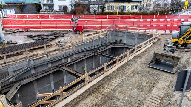 Baustelle mit Grube und Bagger in Wohngebiet.