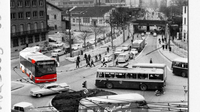 Historische Strassenkreuzung mit Bussen und Autos, Schwarz-Weiss-Foto mit rotem Bus farblich hervorgehoben.