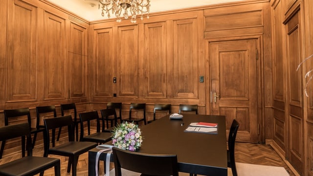 Holzgetäfelter Raum mit Stühlen, Tisch und Blumenstrauss.