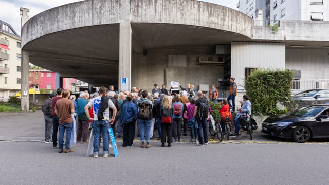 Gruppe von Menschen steht auf einer Strasse vor einem Gebäude.