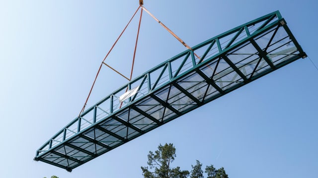 Grosse Metallkonstruktion schwebt an einem Kran am Himmel.