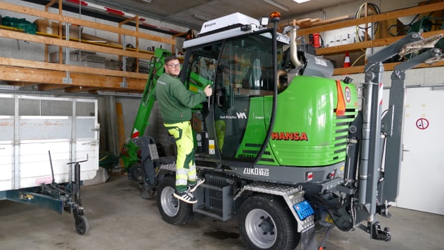 Person in grüner Arbeitskleidung auf grünem Fahrzeug in einer Garage.