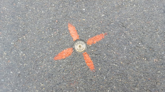 Markierung auf grauem Asphalt mit rotem Kreuzmuster.