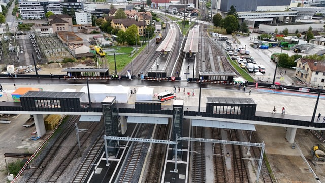 Luftaufnahme eines Bahnhofs mit mehreren Gleisen und Gebäuden im Hintergrund.
