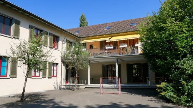 Gebäude mit Innenhof und Bäumen bei sonnigem Wetter.