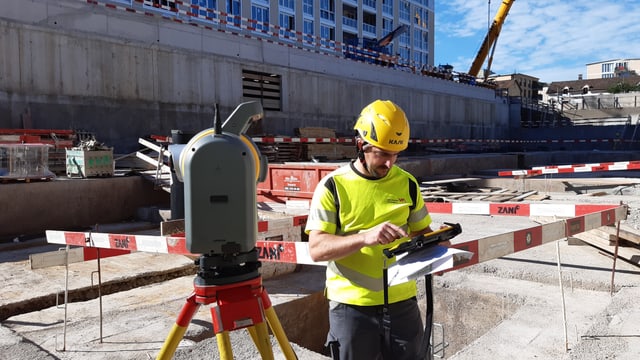 Bauarbeiter mit gelbem Helm bei Baustelle.