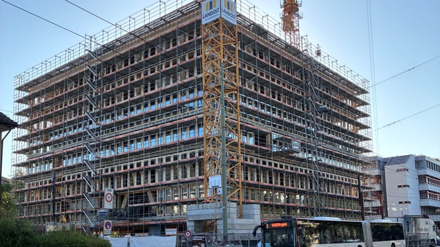 Grosses Gebäude im Bau mit Kränen und vorbeifahrendem Bus.