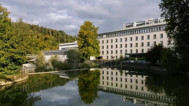 Grosses Gebäude neben einem Fluss mit Baumreflexionen.