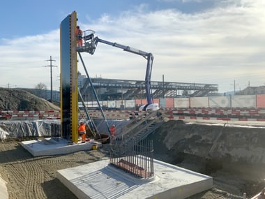Bauarbeiter auf einer Hebebühne neben einer grossen Konstruktion auf einer Baustelle.
