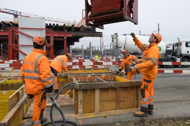 Bauarbeiter in orangefarbenen Schutzanzügen auf einer Baustelle.