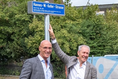 Zwei lächelnde Männer posieren neben einem Strassenschild.