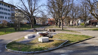 Park mit Bäumen, Gebäuden und einer Feuerstelle.