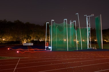 Sportplatz bei Nacht mit Leichtathletiknetz und Lichtspuren.
