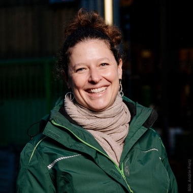 Frau in grüner Jacke lächelnd im Freien.