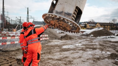 Zwei Personen in orangener Sicherheitskleidung auf einer Baustelle.