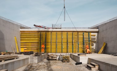 Zwei Bauarbeiter vor einer grossen gelben Schalung an einer Baustelle.