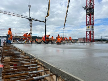 Bauarbeiter in orange Kleidung bei Betonarbeiten auf einer Baustelle.