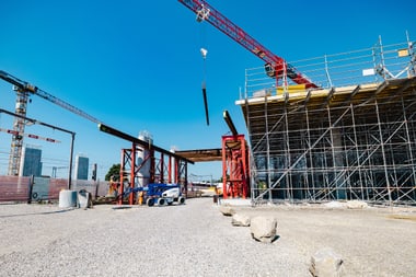 Baustelle mit Kränen und Gerüststruktur unter blauem Himmel.