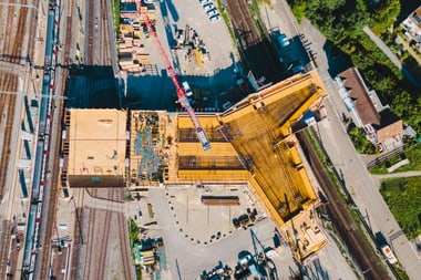 Luftaufnahme einer Baustelle mit Kran neben Bahngleisen.