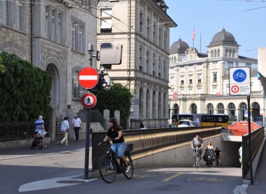 Strassenszene mit Menschen auf Fahrrädern und Fussgängern neben historischen Gebäuden.