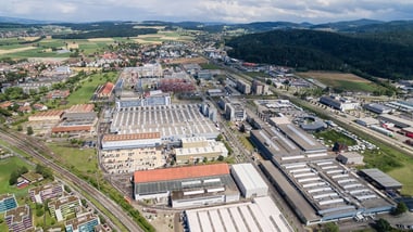 Luftaufnahme eines Industriegebiets mit Gebäuden und Feldern im Hintergrund.