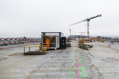 Baustelle mit Kran und Arbeiter in orangefarbener Weste.